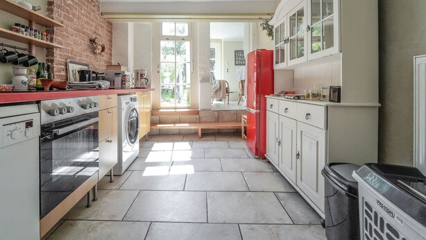 A kitchen with a brick wall, a washing machine, a red refrigerator, and a trash bin.