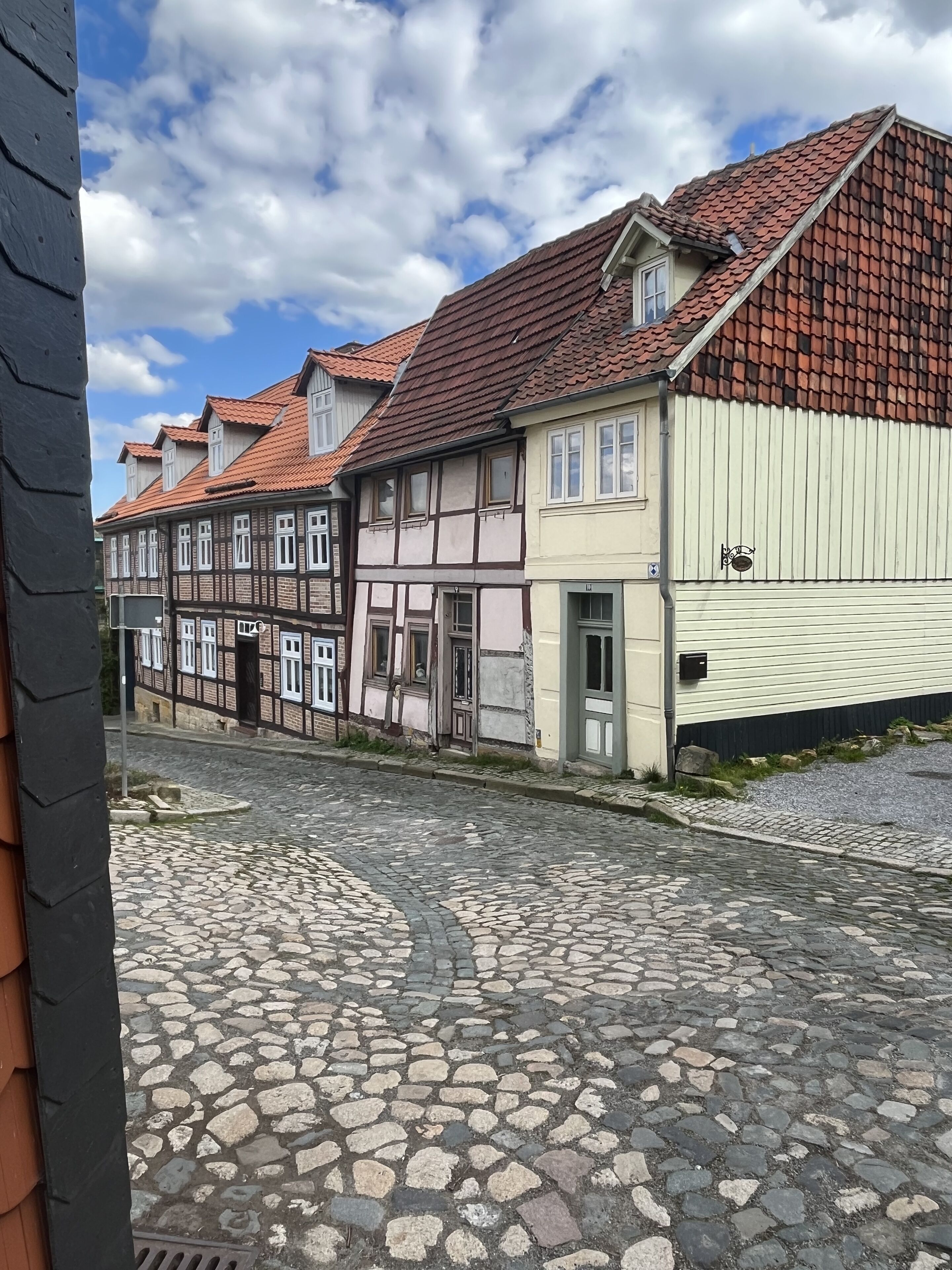 A cobblestone street with traditional half-timbered houses, a gated entrance, and a clear sky.