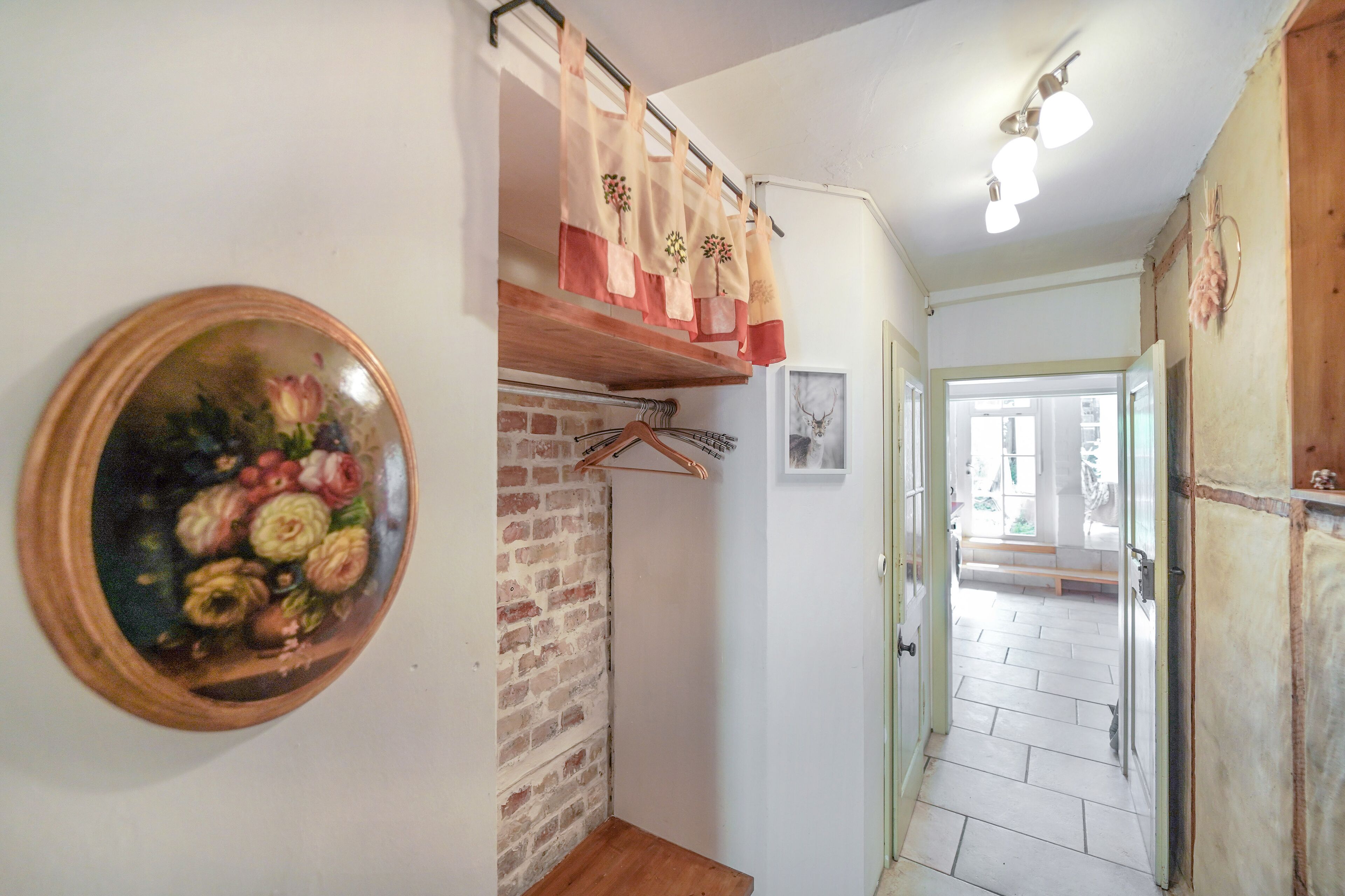 A hallway with a brick wall, a wooden door, and a hanging rack with aprons.