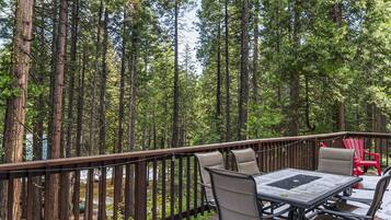 A deck with a table and chairs, surrounded by tall trees.