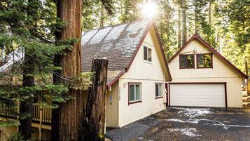 A two-story house with a garage, surrounded by tall trees and a wooden deck.