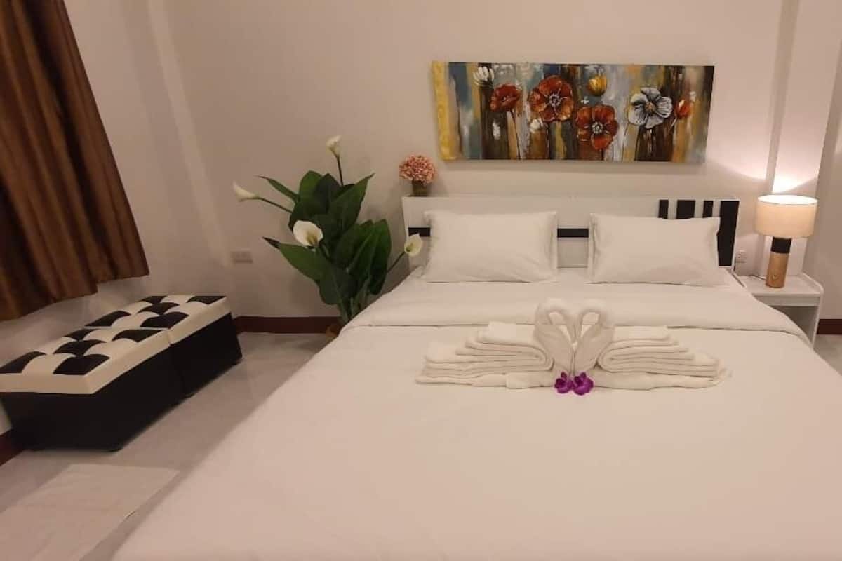 Una habitación de hotel con una cama bien hecha, un cuadro en la pared y una planta en maceta.