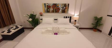 A hotel room with a neatly made bed, a painting on the wall, and a potted plant.