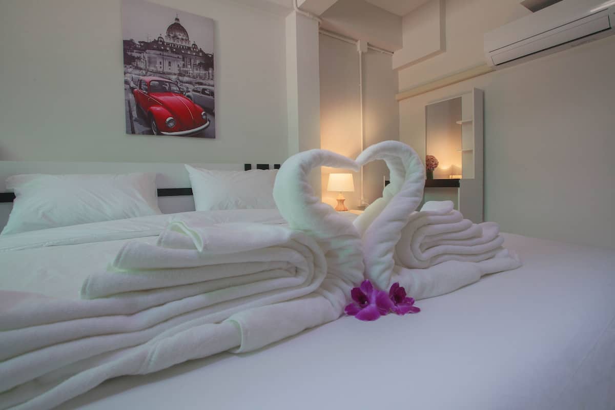 Una cama bien hecha con toallas dobladas en forma de corazón, una lámpara en la mesita de noche y una pared con una fotografía de un coche y un edificio.