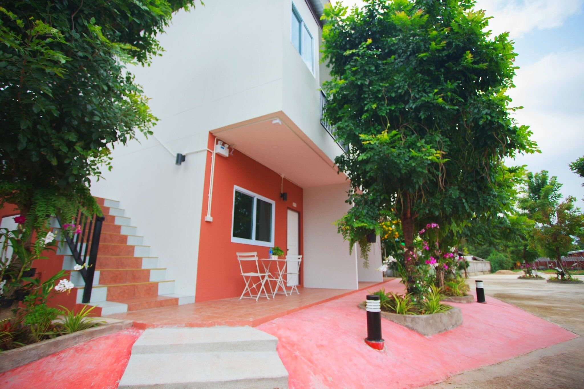 Un edificio moderno con fachada roja y blanca, un acceso cubierto y un pequeño espacio exterior con mesas.