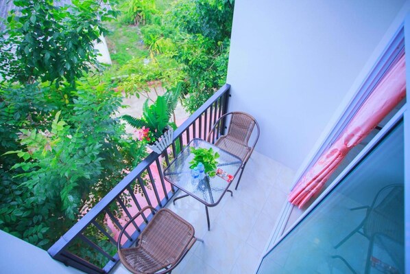 A balcony with a glass table and wicker chairs, surrounded by lush greenery.