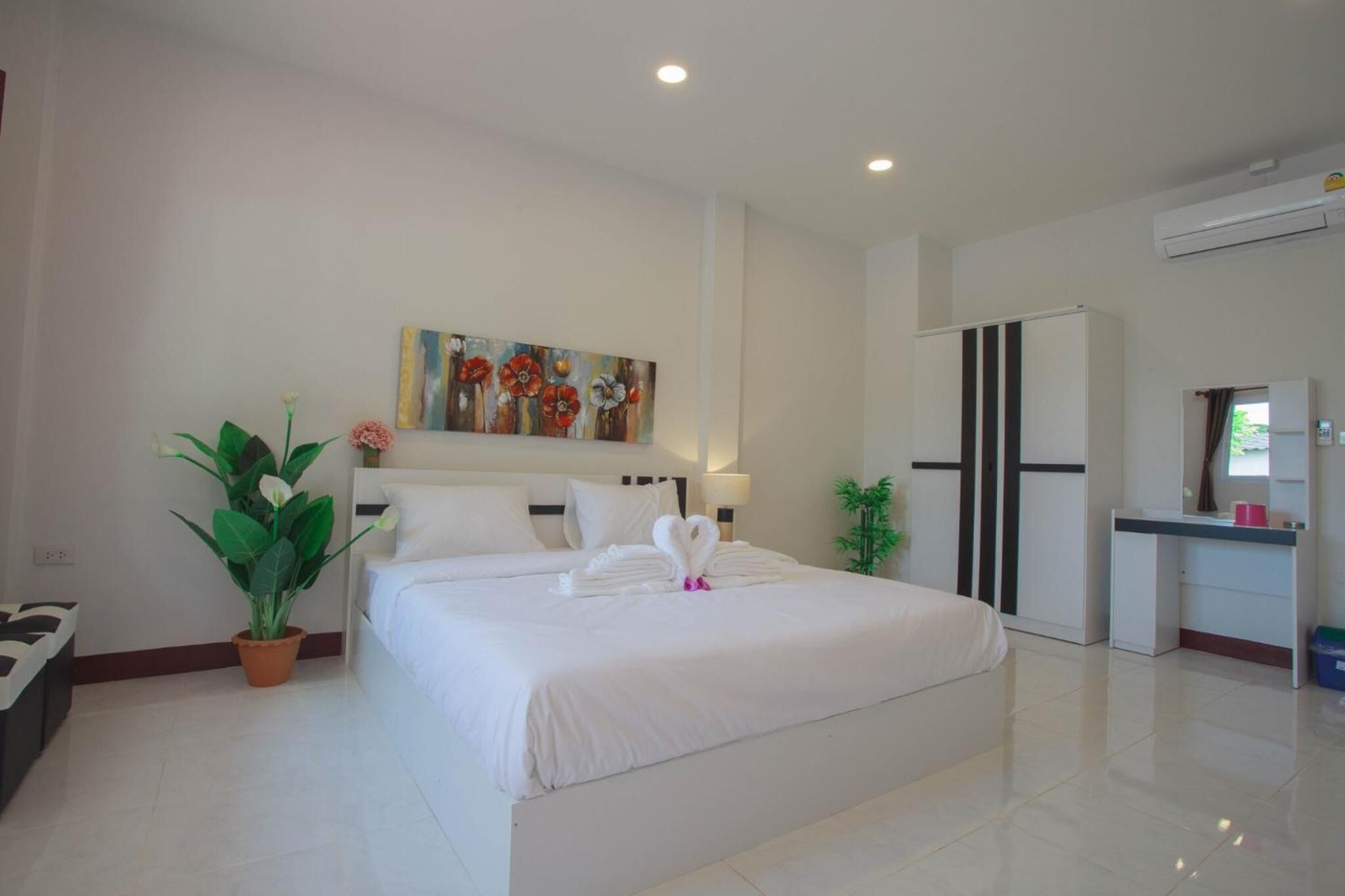 A hotel room with a large bed, a desk, a wardrobe, and a painting on the wall.