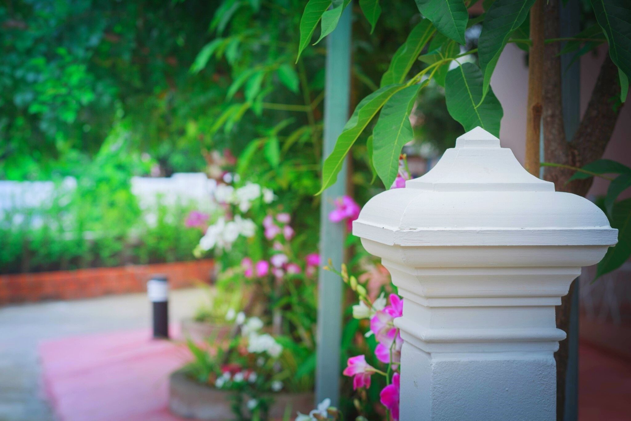 A white column with a decorative top, surrounded by lush greenery and pink flowers.