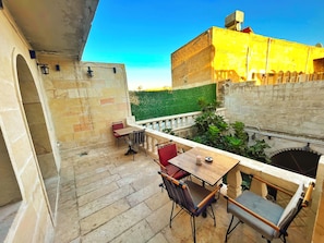 Una terraza con suelo de piedra, una mesa con sillas y vistas a un edificio con pared verde y fachada amarilla.
