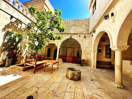 Un patio con suelo de piedra, mobiliario de madera y arcos.