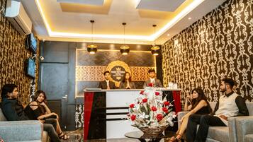 A hotel reception area with a reception desk, a decorative floral arrangement, and seating for guests.