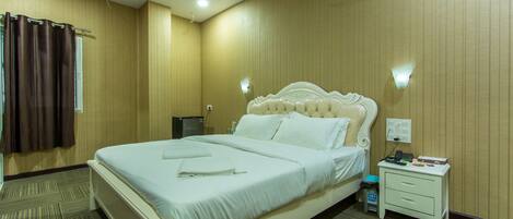 A hotel room with a large bed, a nightstand, a ceiling fan, and a wall-mounted light.