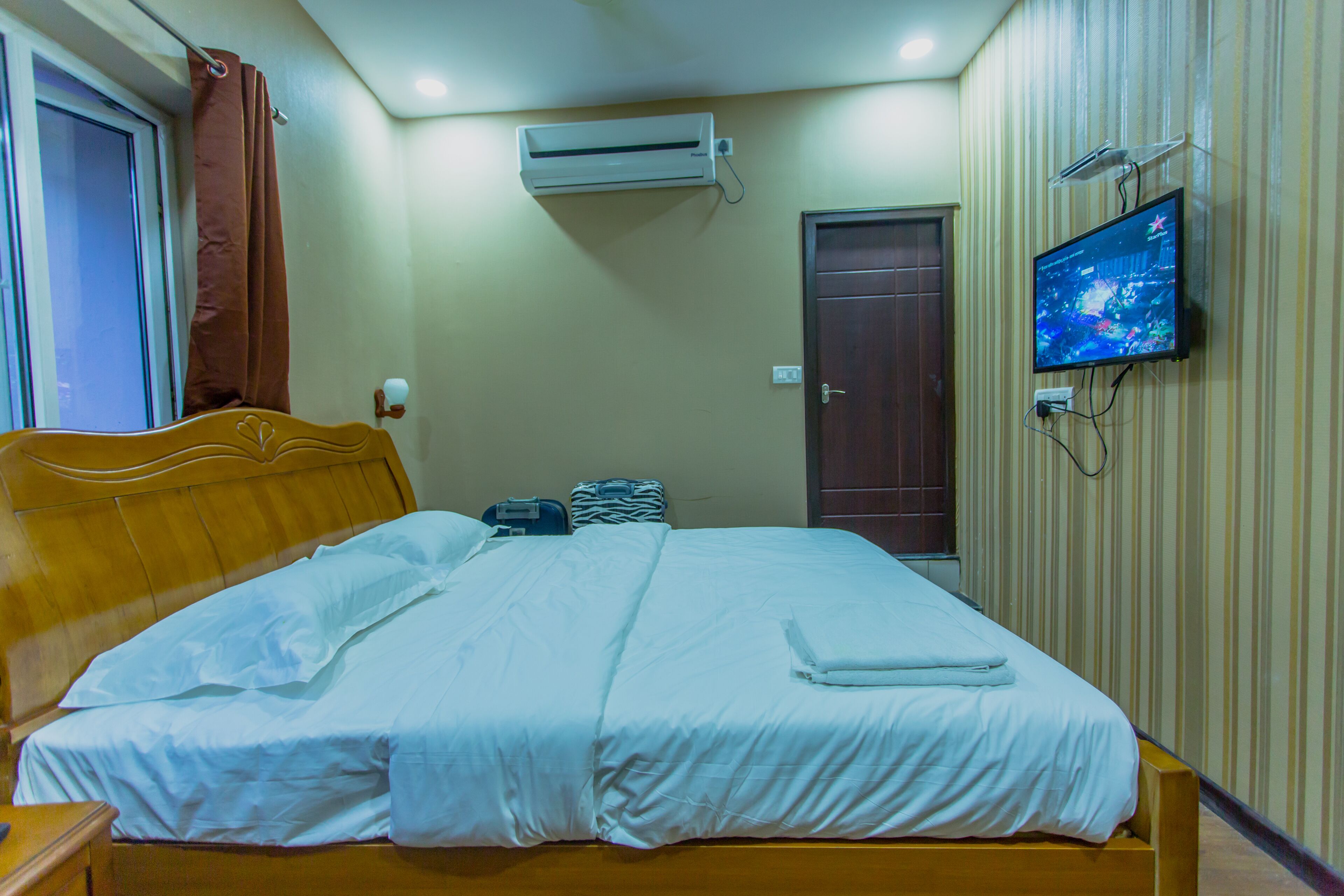 A neatly made bed with white linens, a wooden headboard, and a flat-screen TV mounted on the wall.