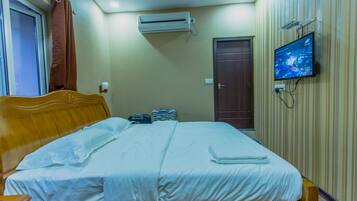 A neatly made bed with white linens, a wooden headboard, and a flat-screen TV mounted on the wall.