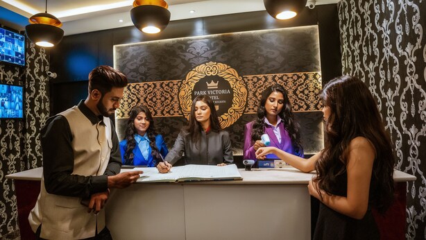 A reception desk at Park Victoria Hotel in Kolkata with a modern design, a crown logo, and a digital screen displaying images. - Hotel Park Victoria (Kolkata)