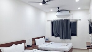 A hotel room with two beds, a ceiling fan, an air conditioning unit, a window with curtains, and a flat-screen TV. - Hotel Park Victoria (Kolkata)