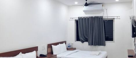 A hotel room with two beds, a ceiling fan, an air conditioning unit, a window with curtains, and a flat-screen TV.