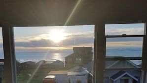 Une vue depuis une fenêtre donnant sur une zone côtière, au moment du coucher du soleil.