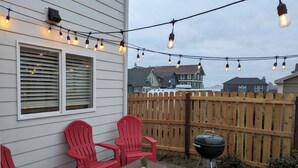 Une terrasse avec des chaises rouges, une table en osier et un barbecue.