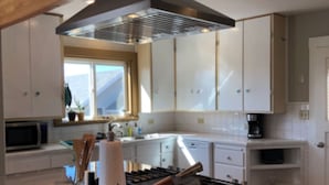 Une cuisine moderne avec des armoires blanches, une hotte en acier inoxydable et un grand îlot central doté d’un plan de travail en verre.