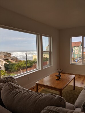 Ein Wohnzimmer mit großem Fenster mit Blick auf den Ozean und die Skyline einer Stadt.