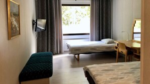 A hotel room with two beds, a desk, a chair, a bench, a flat-screen TV, and a window with curtains. - Hotelli Äänekoski (Äänekoski)