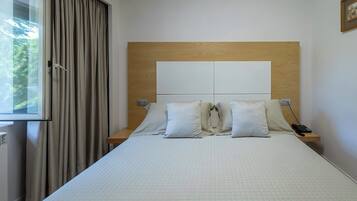 Habitación de hotel con una cama grande, dos mesitas de noche, una ventana con cortinas y un cabecero de madera.