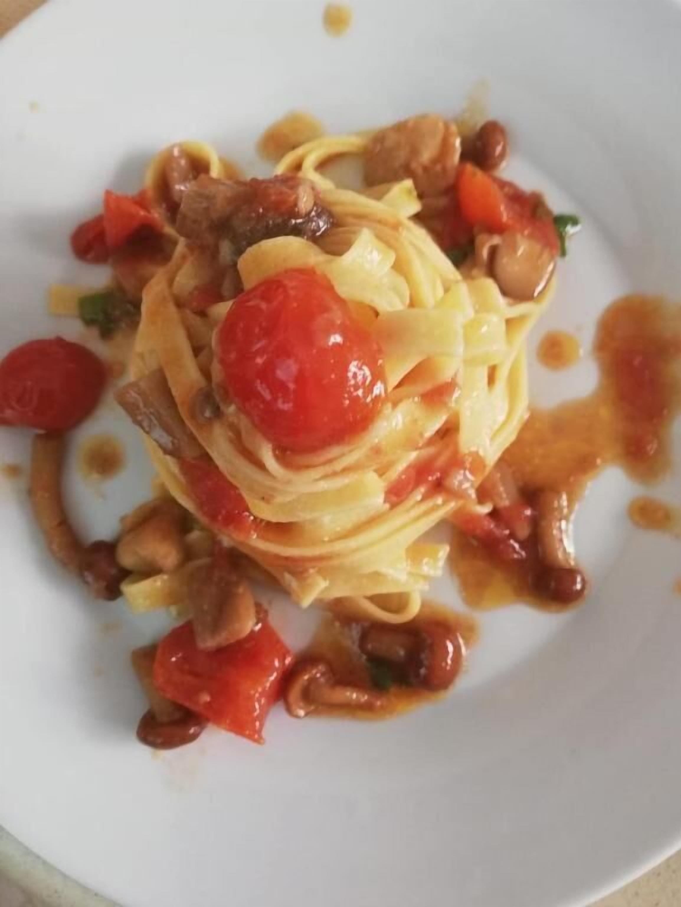A plate of pasta with cherry tomatoes and a drizzle of sauce.