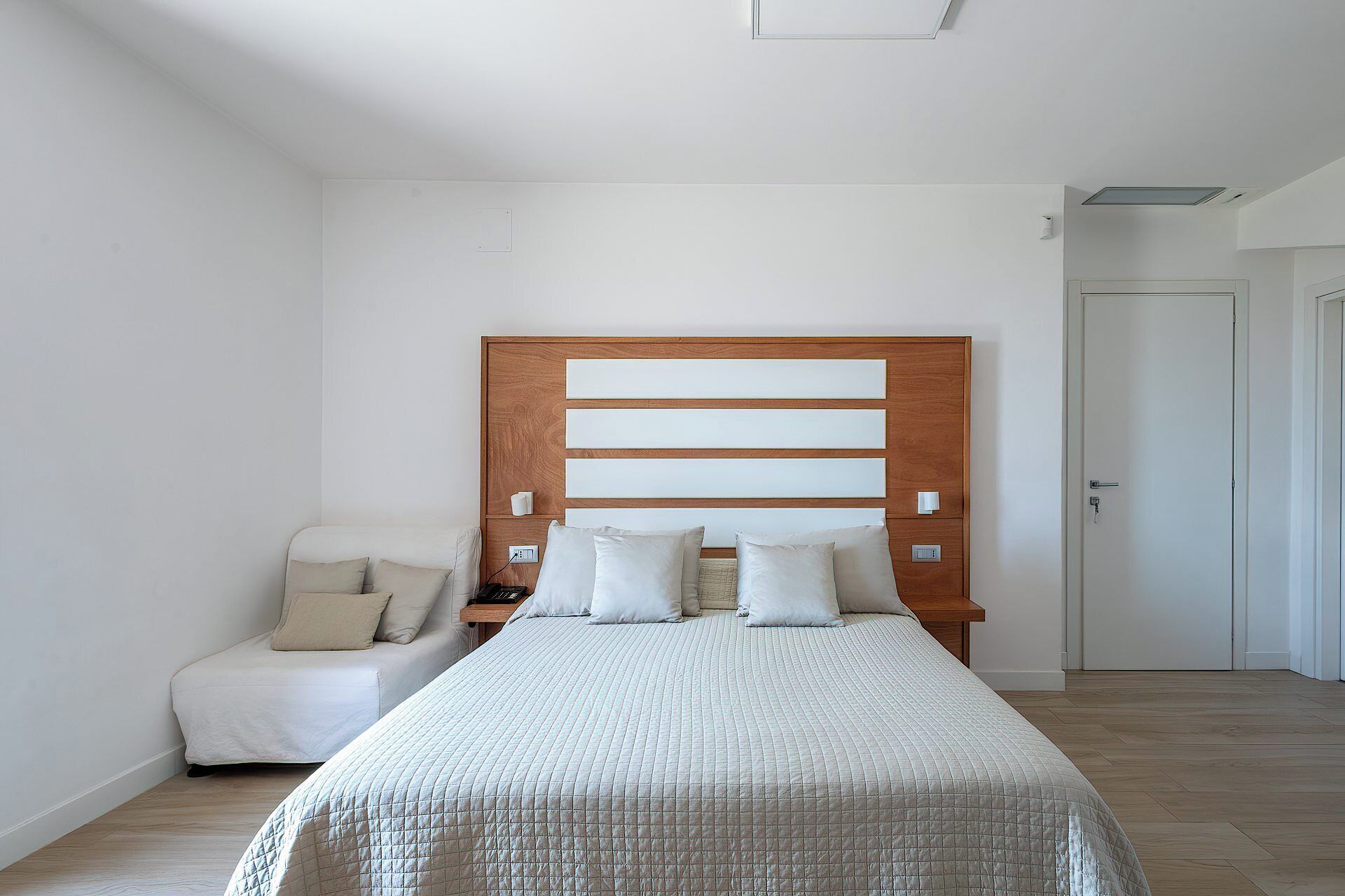 A bedroom with a large bed, a bedside table, a chair, and a wardrobe.
