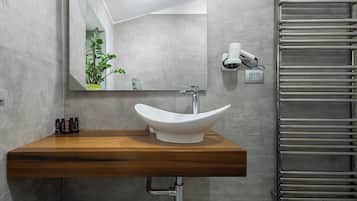 A bathroom with a white vessel sink, a wooden countertop, a mirror, a towel dispenser, and a towel rack.