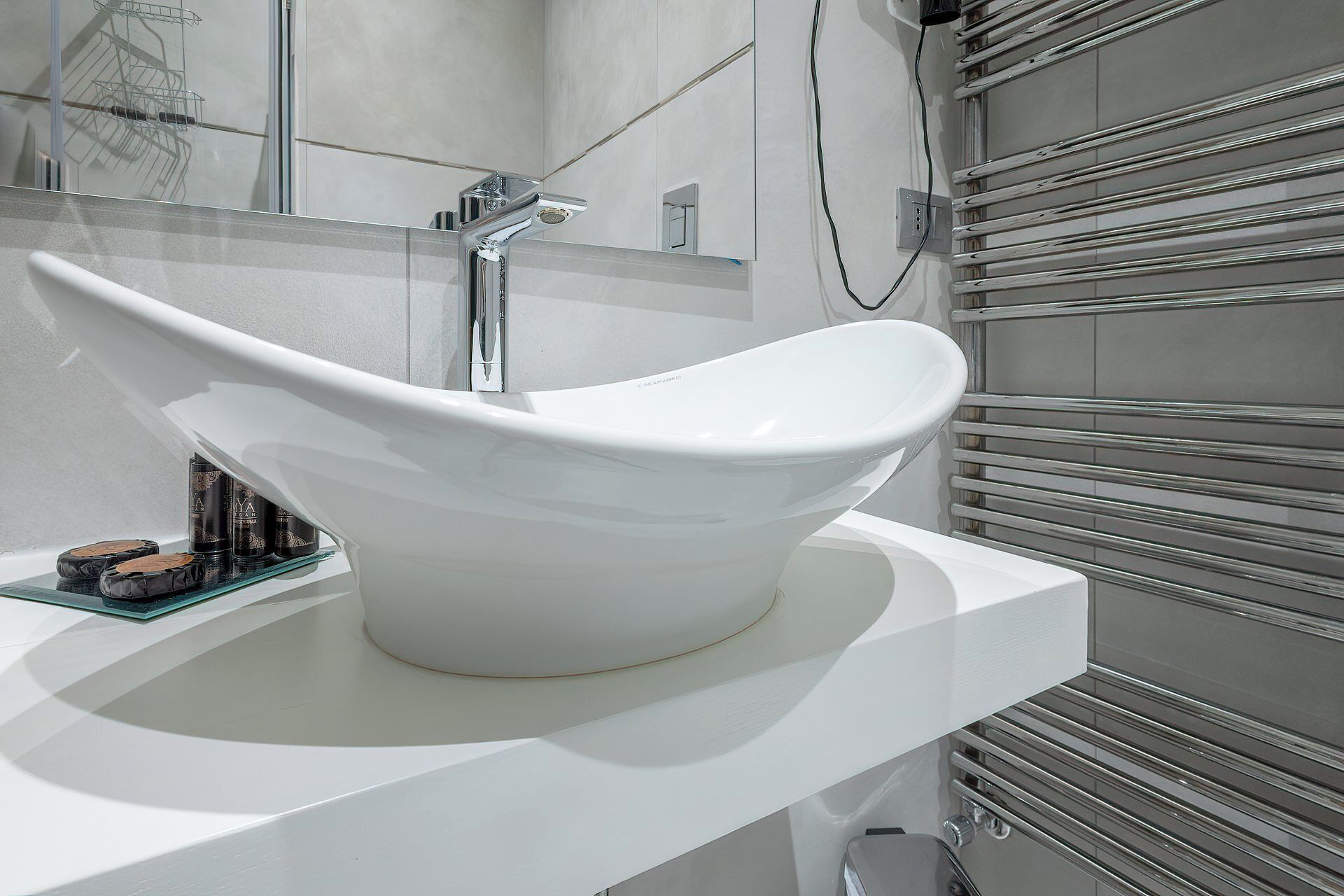 Ein modernes Badezimmer mit einem weißen Waschbecken, einem Chromarmaturen-Set und einer Glasablage für Pflegeartikel.