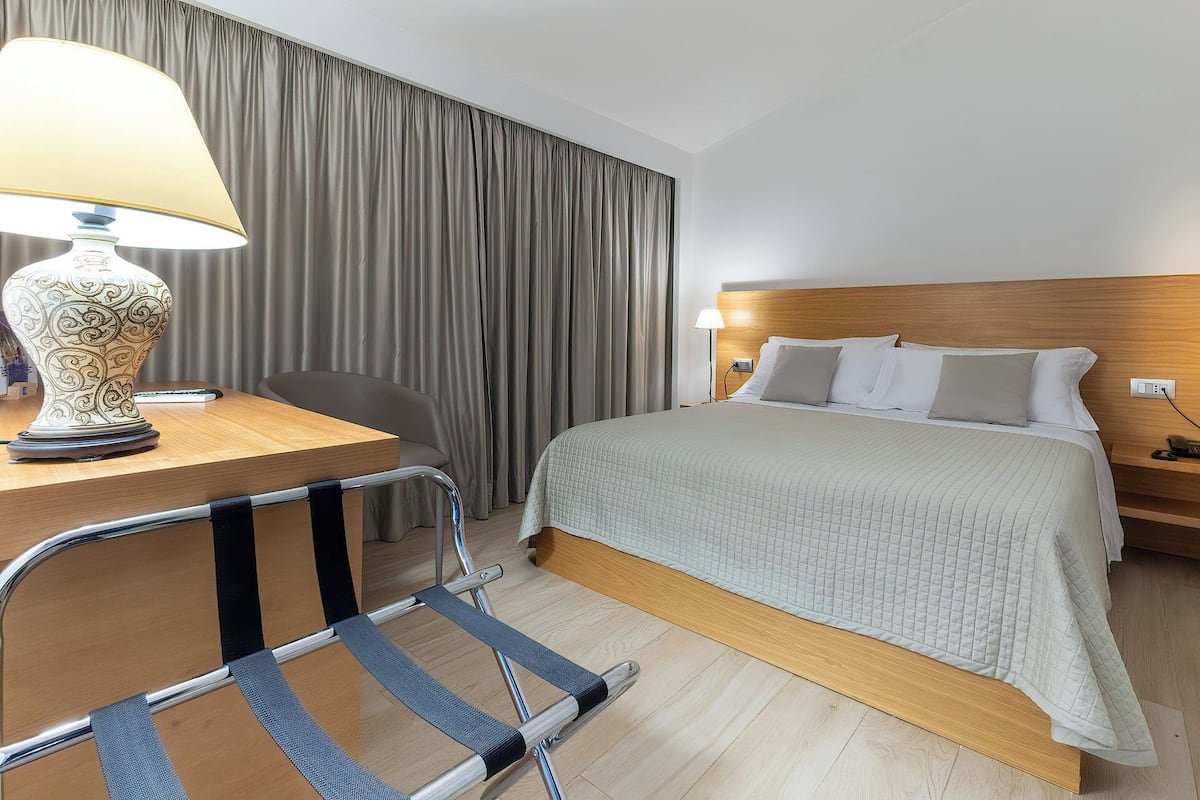 Une chambre d’hôtel avec un lit, une table de chevet, une lampe, une chaise et des rideaux.