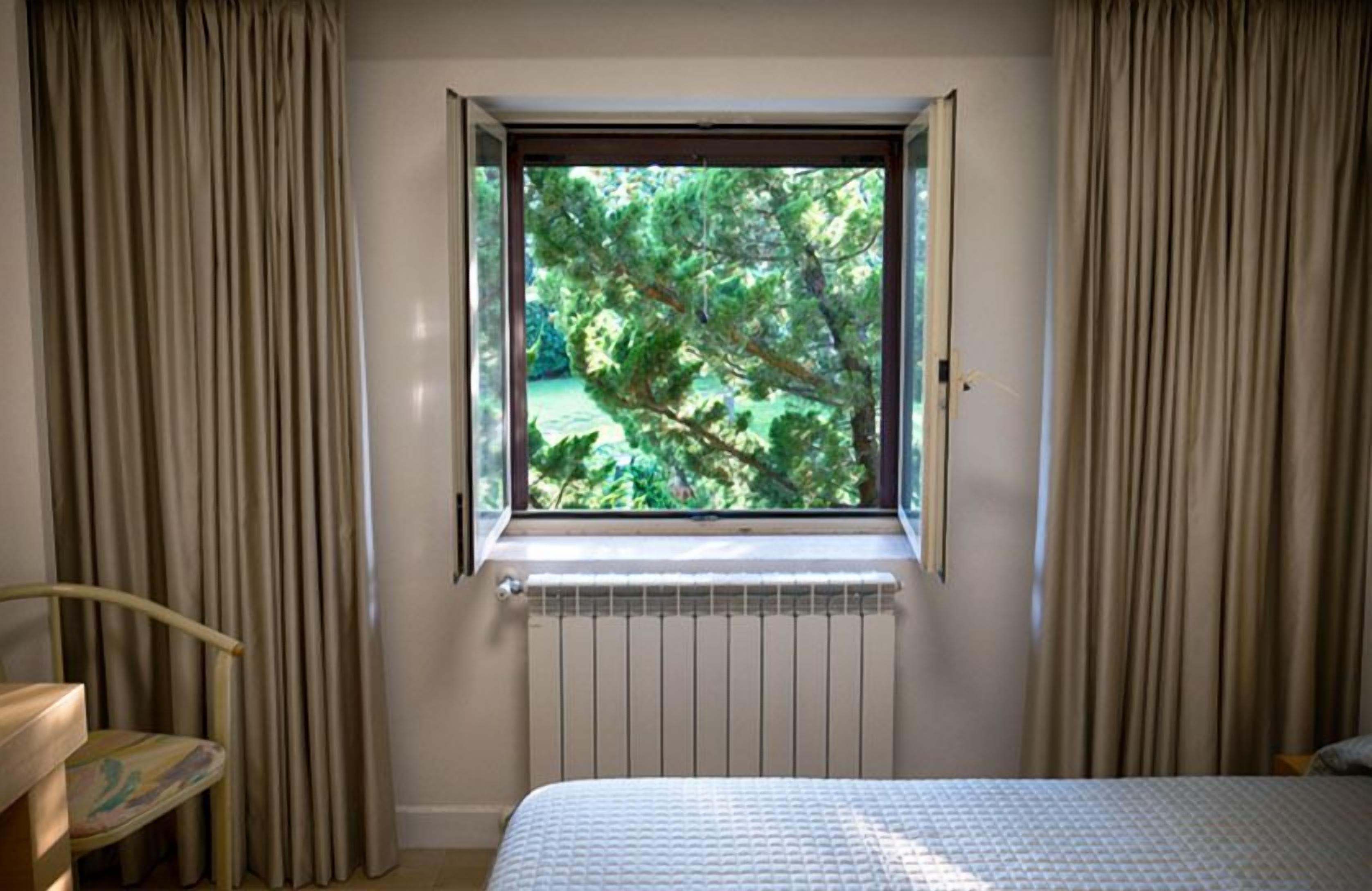 Un dormitorio con ventana, cortinas, radiador y cama.