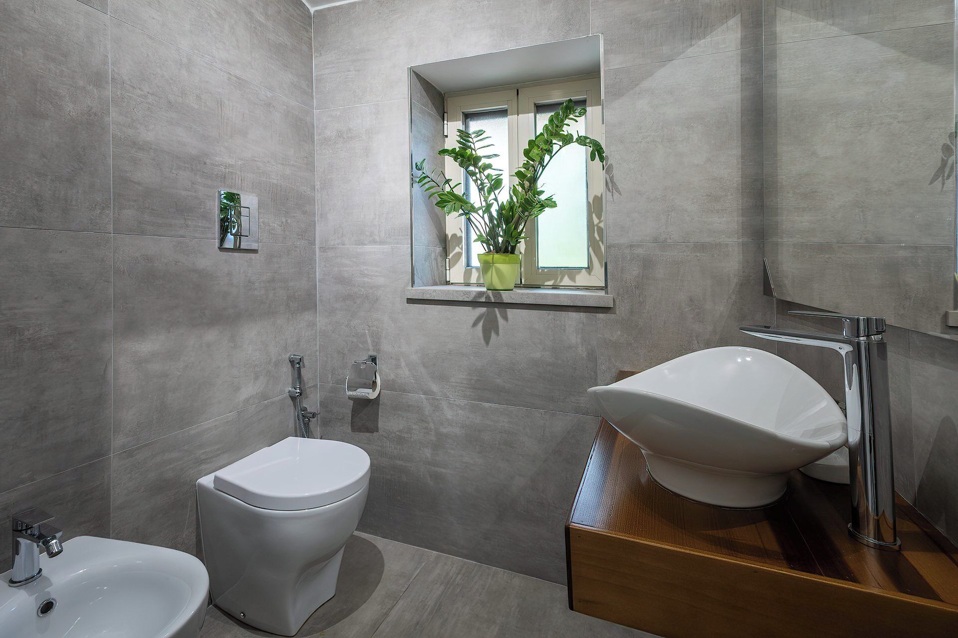 A modern bathroom with a bidet, a sink, and a window with a potted plant.