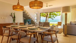 A modern dining area with a large table set for six, wooden chairs, and a view of the ocean through large windows. - Manta Cove by Horizon Holidays (Black River)