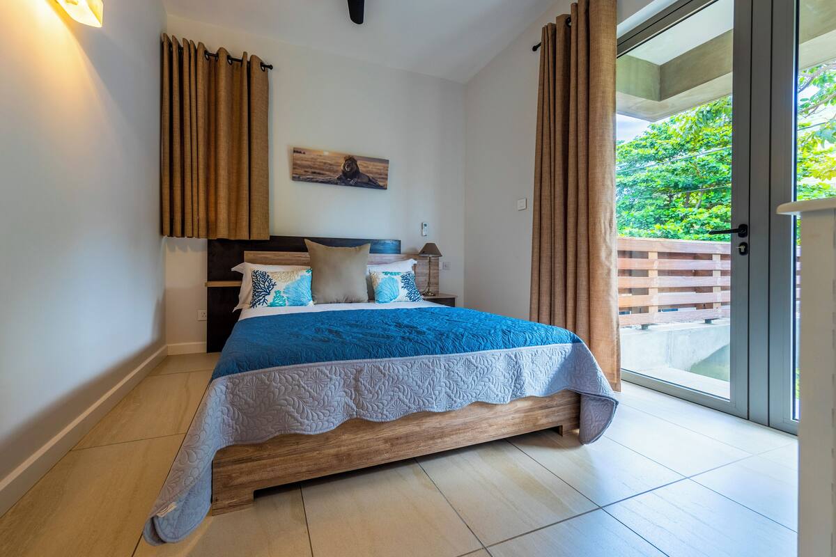 A bedroom with a wooden bed, a view of greenery through a sliding door, and a painting on the wall.
