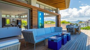A modern outdoor living area with a blue sofa, wooden deck, and a view of mountains. - Manta Cove by Horizon Holidays (Black River)