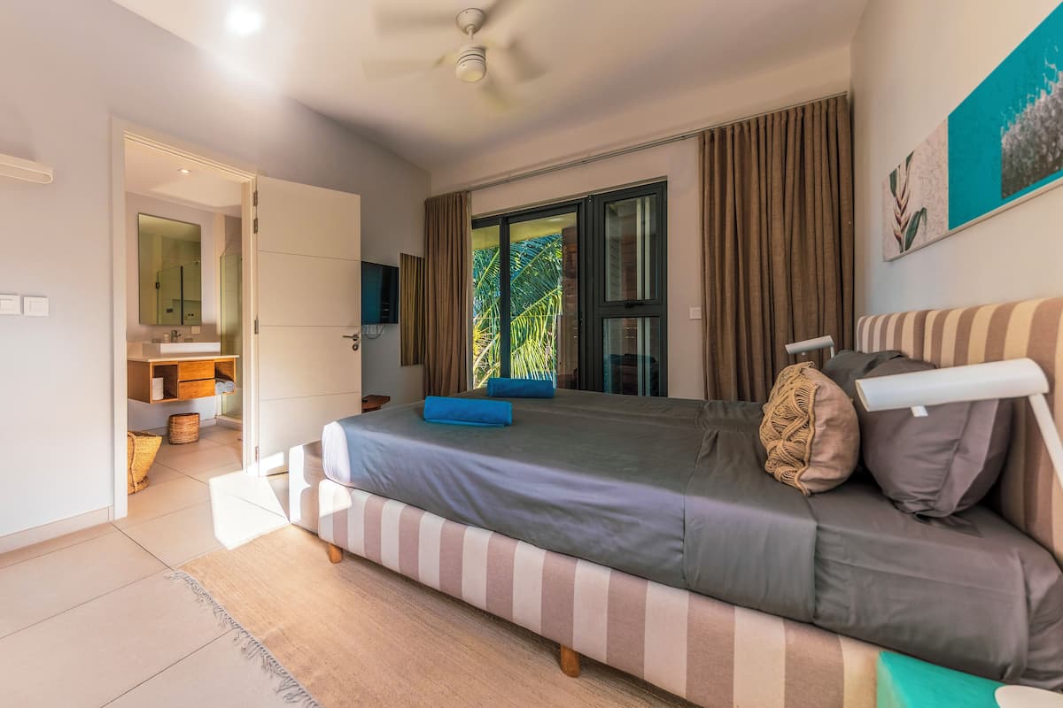 A modern bedroom with a large bed, a TV, and a bathroom visible through an open door.