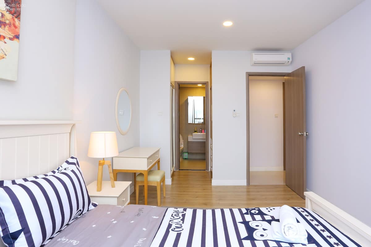 A bedroom with a bed, bedside table, lamp, and a view of the bathroom through an open door.