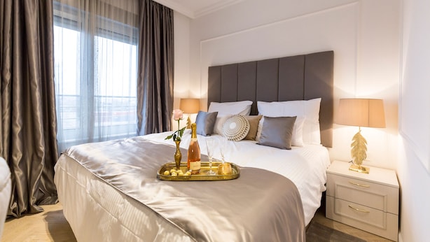 A neatly made bed with a tray of snacks, a bottle, and glasses, a bedside lamp, and a window with curtains. - MM House - Adults Only (Zagreb)