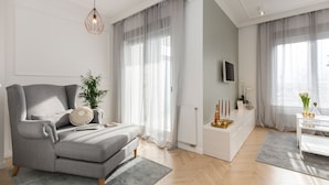 A modern living room with a grey sofa, a white side table, and a large window with sheer curtains. - MM House - Adults Only (Zagreb)