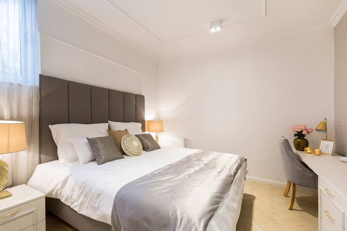 A modern bedroom with a large bed, bedside tables, a desk, and a chair.