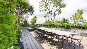 An outdoor dining area with a long table and chairs, surrounded by lush greenery and trees. - Ami Splendid Rooftop Garden (Ho Chi Minh City)
