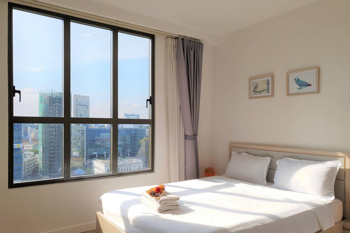 A hotel room with a large window, a bed with white linens, and two framed pictures on the wall.