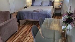 A bedroom with a bed, bedside tables, a nightstand, a glass table, a chair, a sofa, an air conditioning unit, and a window with curtains. - Private access, remote gate.  Netflix,  Foxtel,  Wi-Fi,  A/C, (Broken Hill)