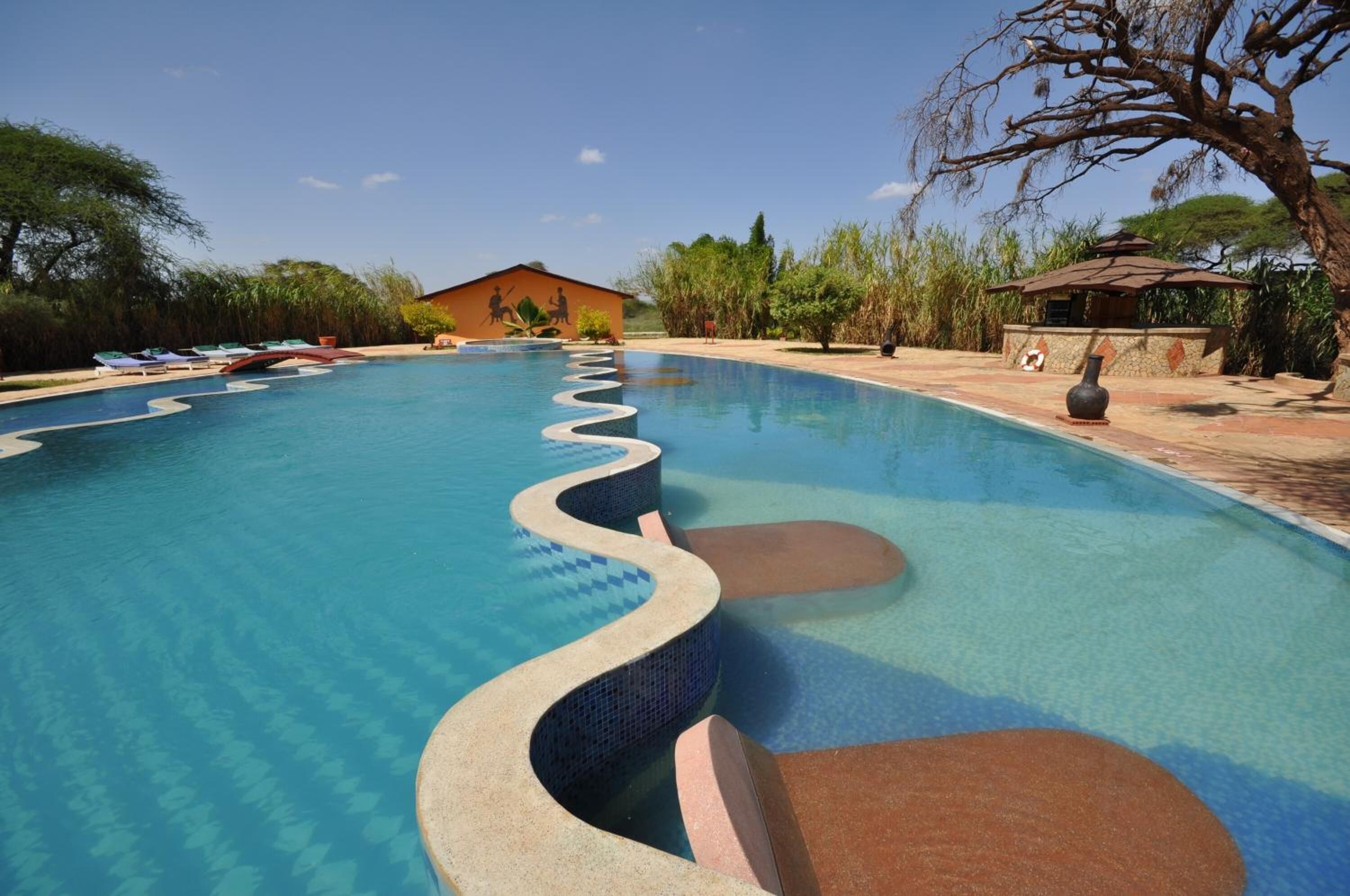 A swimming pool with a wavy edge design, surrounded by lounge chairs and a small pavilion.