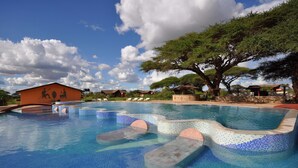 A swimming pool with mosaic tiles, lounge chairs, and a building with a mural.
