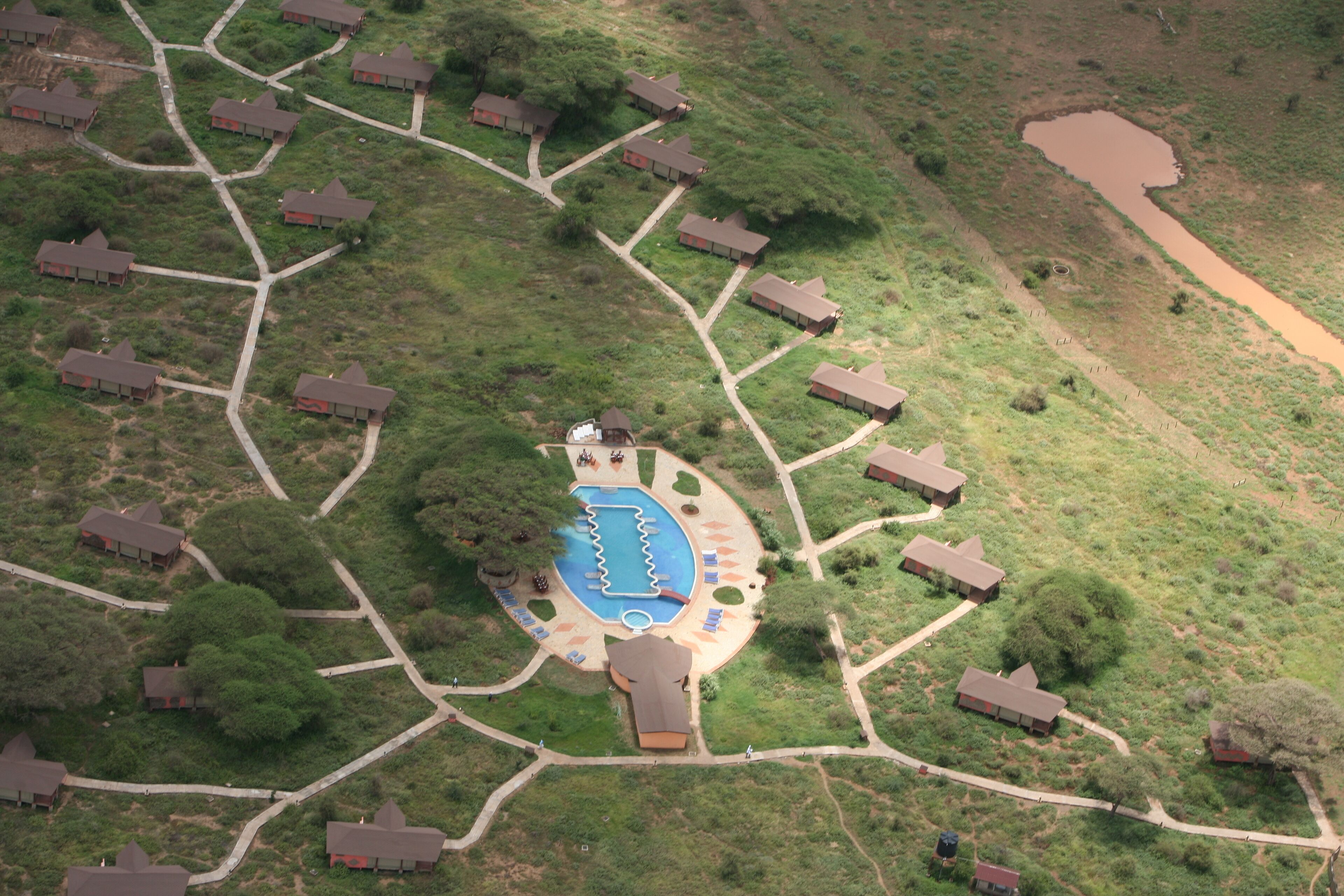 Vista aérea de un complejo turístico con una piscina central, rodeado de cabañas de huéspedes conectadas por senderos.