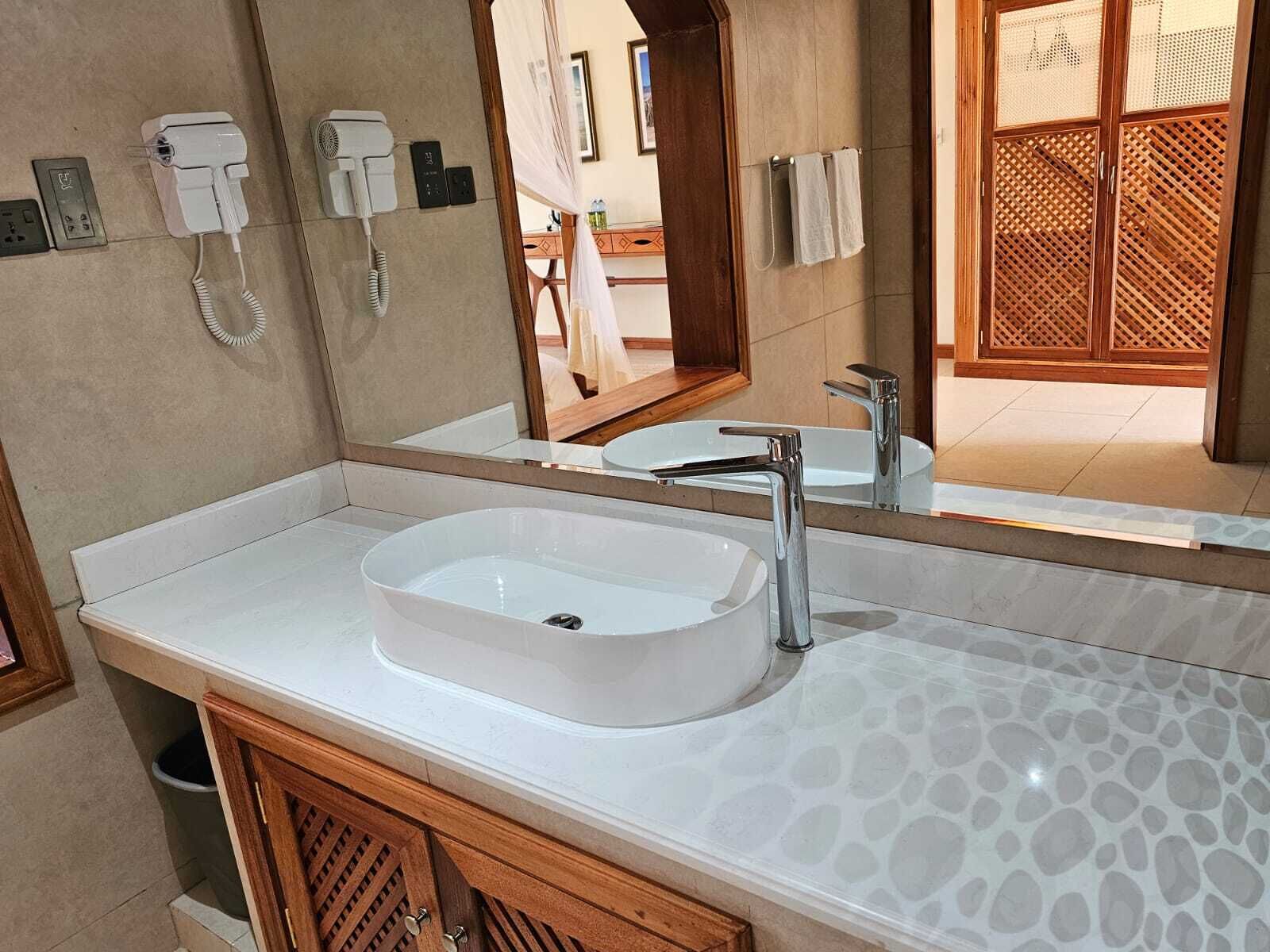 Une salle de bain avec un lavabo blanc, un miroir, un sèche-cheveux et un téléphone fixé au mur.