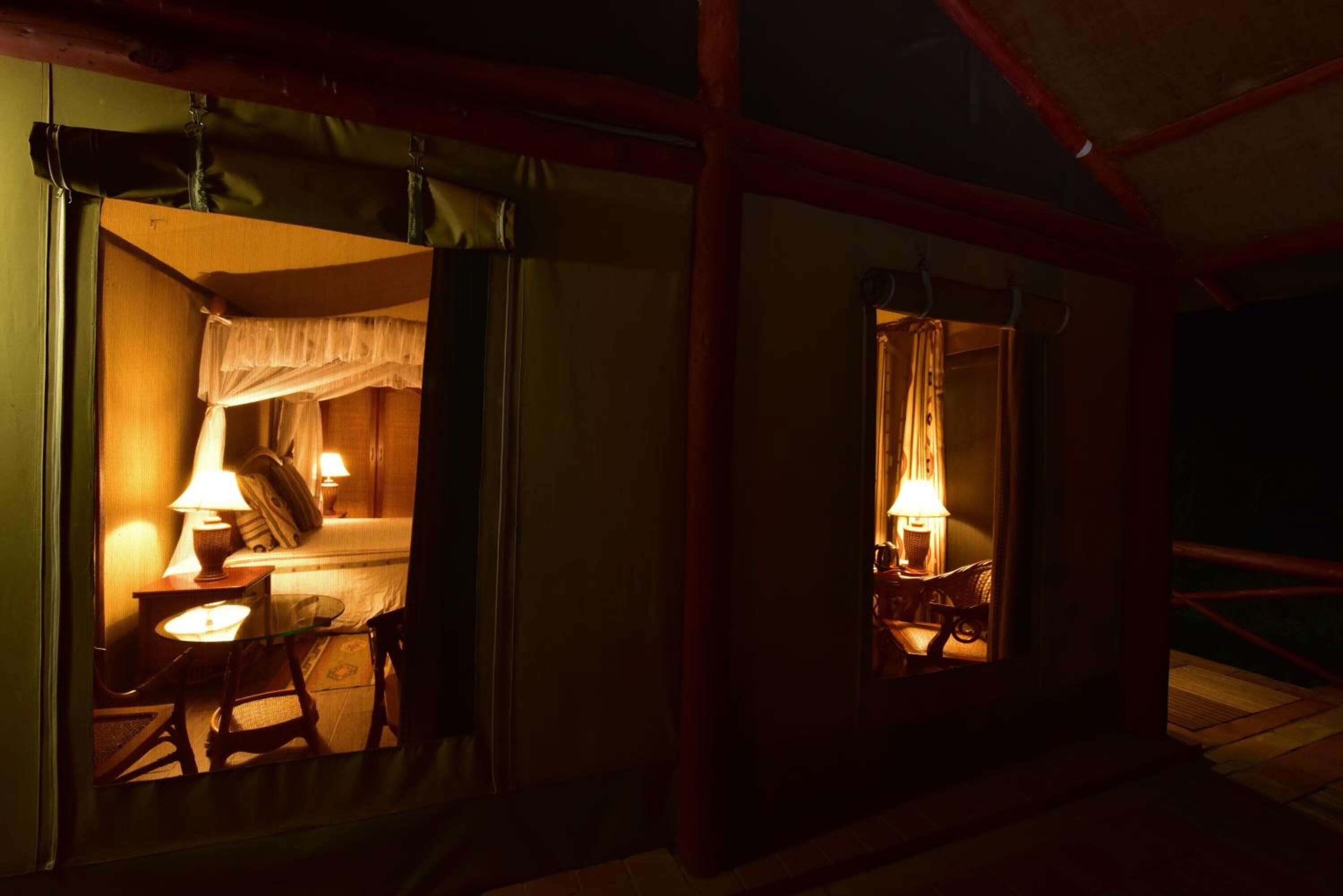 Um quarto com pouca luz, com uma cama, uma cadeira, uma mesa e um abajur.